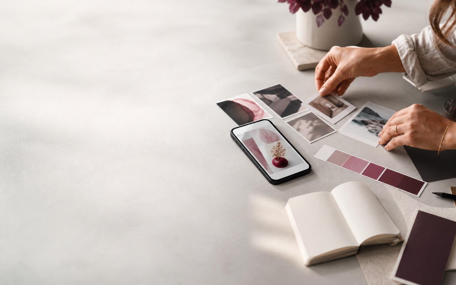 Hands arranging photo selections, color references, a phone, and a notebook on a creative worktable